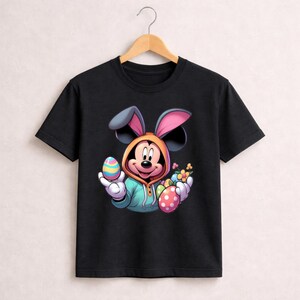 May include: Black t-shirt featuring a cartoon Mickey Mouse character dressed as an Easter bunny. Mickey is wearing a hooded sweatshirt and holding colorful Easter eggs and flowers. The design is vibrant and playful, perfect for Easter celebrations.