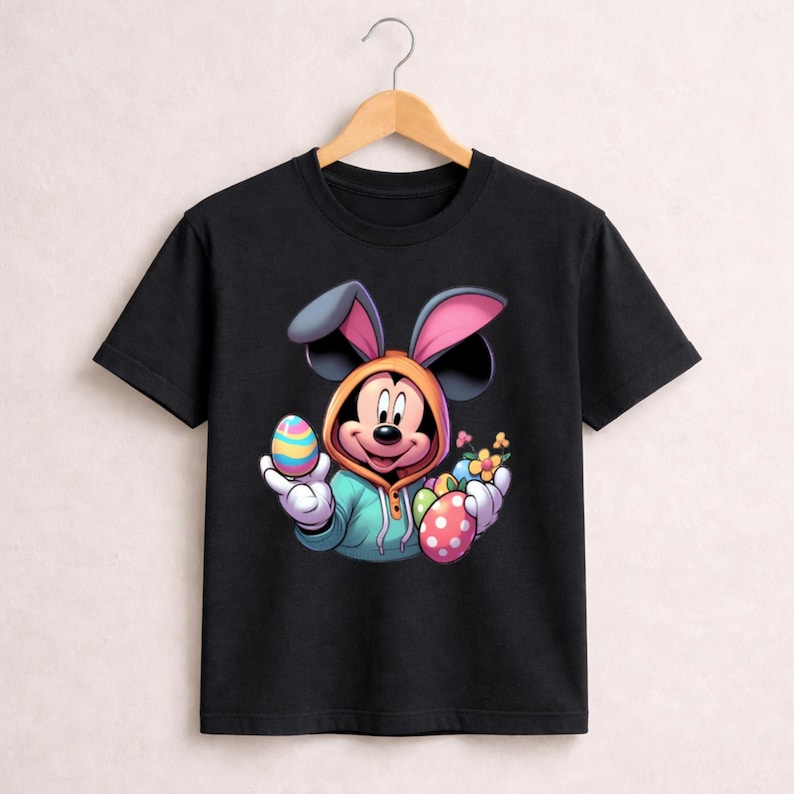 May include: Black t-shirt featuring a cartoon Mickey Mouse character dressed as an Easter bunny. Mickey is wearing a hooded sweatshirt and holding colorful Easter eggs and flowers. The design is vibrant and playful, perfect for Easter celebrations.