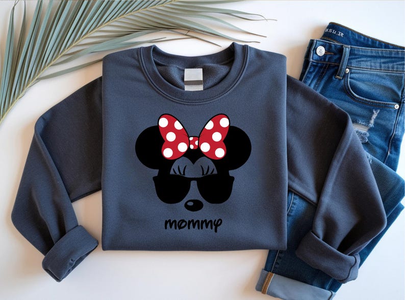 Może przedstawiać: Granatowa bluza z nadrukiem Myszki Minnie. Wz&oacute;r zawiera czerwoną kokardę w białe grochy, czarne okulary przeciwsłoneczne i napis "mamusia". Bluza jest połączona z niebieskimi dżinsami.