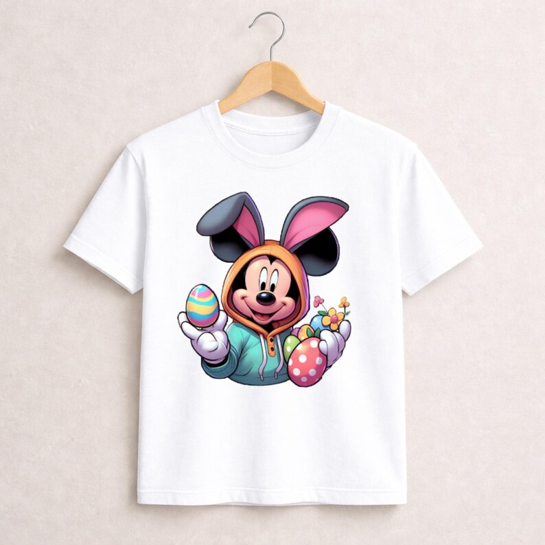 May include: White t-shirt featuring a cartoon Mickey Mouse character dressed as an Easter bunny. Mickey is wearing a hooded sweatshirt and holding colorful Easter eggs and flowers. The design is vibrant and playful, perfect for Easter.