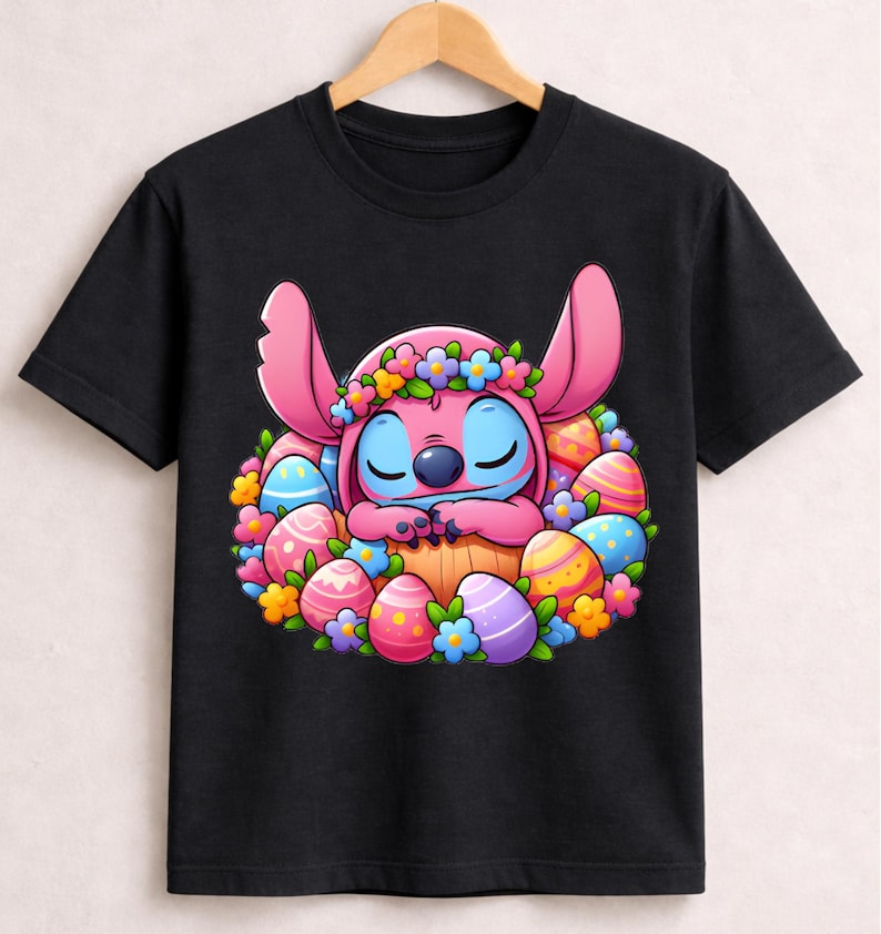 May include: Black t-shirt featuring a cartoon character with pink ears and blue skin, surrounded by colorful Easter eggs and flowers. The character is wearing a flower crown and is nestled in a basket. A fun, festive design for Easter.