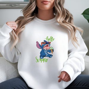 Puede incluir: Sudadera blanca con un personaje de dibujos animados Stitch con gafas de sol y un helado. Las palabras "hello Summer" est&aacute;n escritas en verde. La sudadera es de estilo casual.