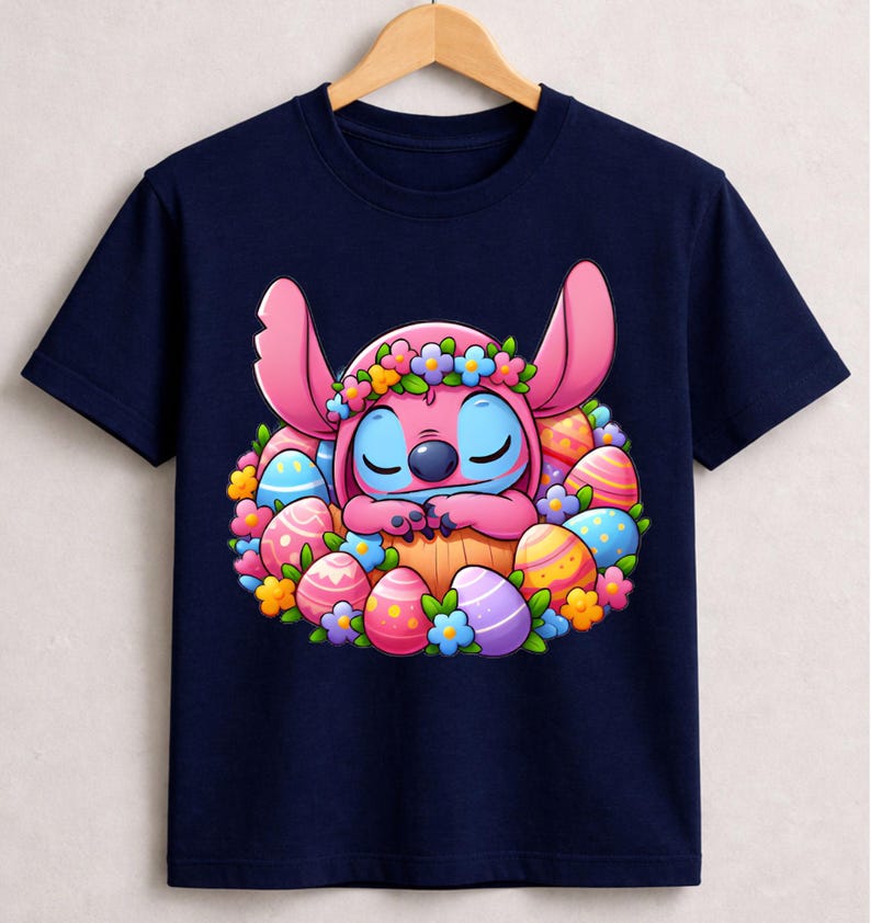 May include: Navy blue t-shirt featuring a cartoon character with pink ears and blue eyes, surrounded by colorful Easter eggs and flowers. The character is wearing a flower crown. The design is centered on the shirt.