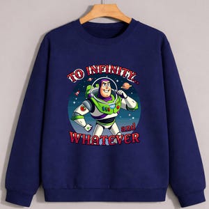 Op de afbeelding: Marineblauwe sweatshirt met een afbeelding van Buzz Lightyear uit Toy Story. Het ontwerp bevat de tekst "TO INFINITY... and WHATEVER" in rode en witte letters. Buzz is afgebeeld in zijn groene en witte ruimtepak, tegen een sterrenachtergrond.