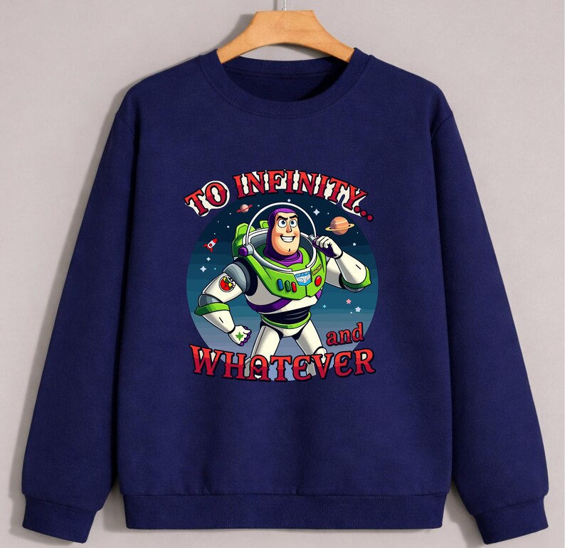 Op de afbeelding: Marineblauwe sweatshirt met een afbeelding van Buzz Lightyear uit Toy Story. Het ontwerp bevat de tekst "TO INFINITY... and WHATEVER" in rode en witte letters. Buzz is afgebeeld in zijn groene en witte ruimtepak, tegen een sterrenachtergrond.