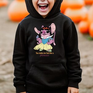 May include: Black hooded sweatshirt featuring a cartoon character in a Snow White-inspired outfit, holding a small object. The text "You make me feel like a princess" is printed below the graphic. The sweatshirt has a front pocket.