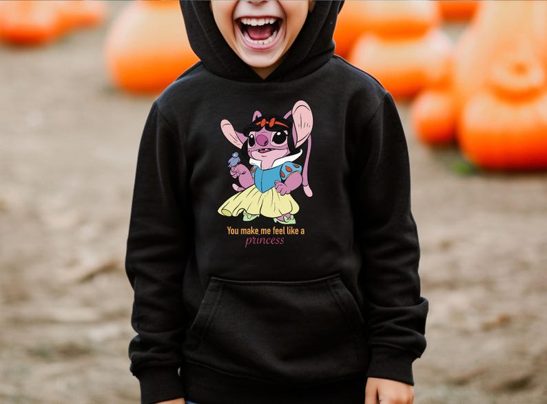 May include: Black hooded sweatshirt featuring a cartoon character in a Snow White-inspired outfit, holding a small object. The text "You make me feel like a princess" is printed below the graphic. The sweatshirt has a front pocket.