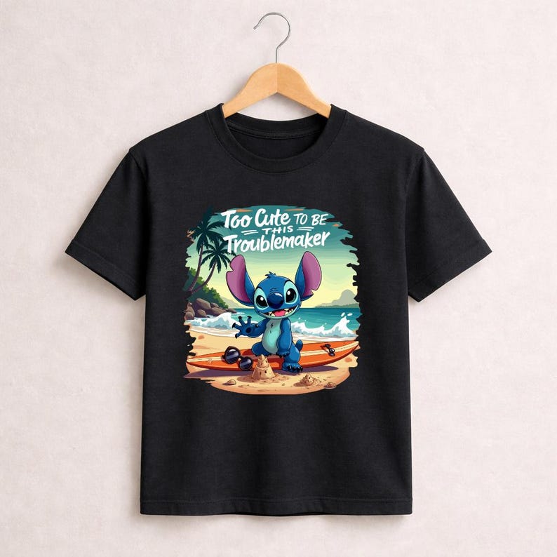 Pu&ograve; includere: T-shirt nera con un personaggio dei cartoni animati su una tavola da surf sulla spiaggia. Il personaggio &egrave; blu con grandi orecchie e sorride. Il testo "Too Cute to be this Troublemaker" &egrave; sopra il personaggio.