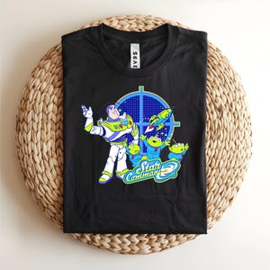 May include: Black t-shirt featuring Buzz Lightyear and the Little Green Men from Toy Story. The design includes the words "Star Command" in a blue and green font, with a blue target graphic and a rocket ship.