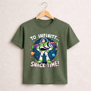 May include: Green t-shirt featuring Buzz Lightyear from Toy Story. The graphic shows Buzz in his spacesuit with the text "TO INFINITY... AND SNACK TIME!" against a starry background. The shirt is hanging on a wooden hanger.