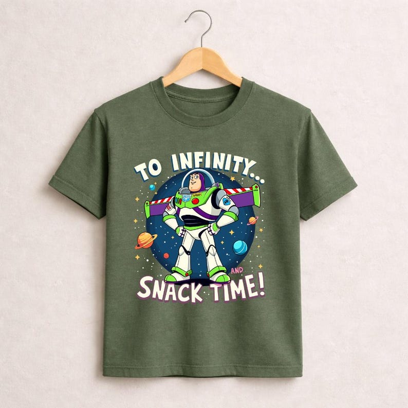 May include: Green t-shirt featuring Buzz Lightyear from Toy Story. The graphic shows Buzz in his spacesuit with the text "TO INFINITY... AND SNACK TIME!" against a starry background. The shirt is hanging on a wooden hanger.