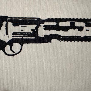 May include: A black graphic print of a revolver handgun on a light-colored fabric background. The design features a detailed silhouette of the firearm with a textured grip, a trigger guard, and a long barrel with a top rail mount.