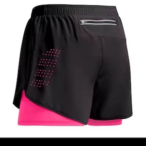 Puede incluir: Pantalones cortos de running negros con un forro interior rosa brillante. Los pantalones cortos tienen un pequeño bolsillo con cremallera en la parte trasera y un diseño de puntos rosas. La cintura es elástica.