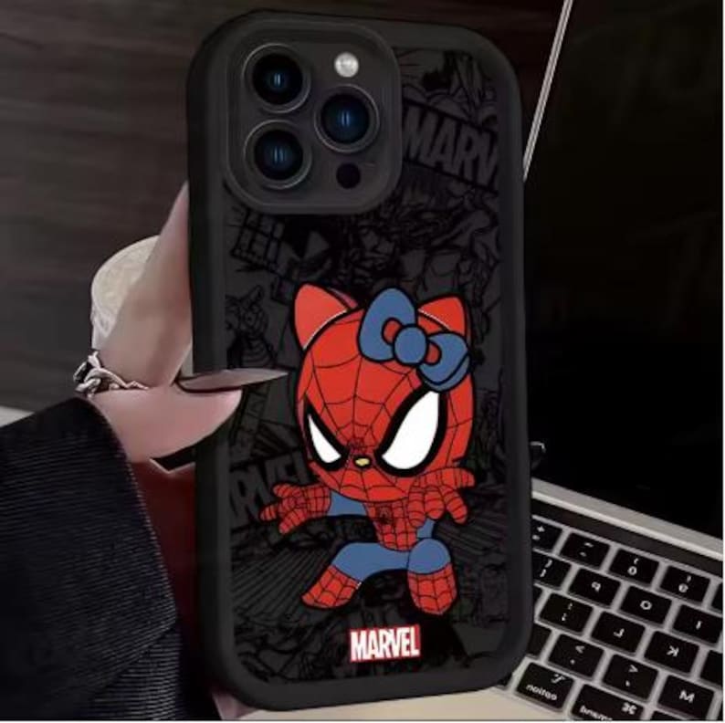 May include: Black phone case featuring a cartoon Spider-Man character with a Hello Kitty-inspired design. The case has a red and blue color scheme, with the Marvel logo at the bottom. The background has a comic book style.