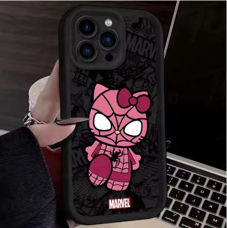 May include: Black phone case featuring a pink cartoon character with a spiderweb design and a bow. The case has a Marvel logo at the bottom. The background has a comic book style design.