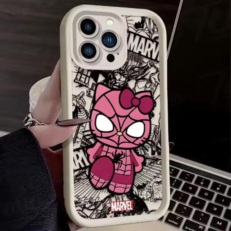 May include: A white phone case featuring a pink Hello Kitty character in a Spider-Man costume. The case has a black and white comic book style background with the word "MARVEL" and the Marvel logo.