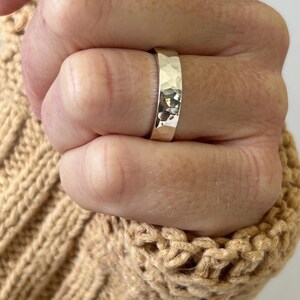 May include: A silver hammered band ring worn on a hand. The ring is wide and has a textured surface.