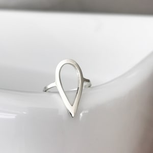 Op de afbeelding: Een zilveren ring in de vorm van een traan met een uitgesneden ontwerp. De ring ligt op een wit oppervlak.