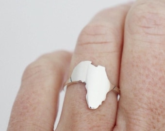 Op de afbeelding: Een ring van gepolijst zilver met een platte, uitgesneden silhouet van het Afrikaanse continent als middelpunt. Het metaal heeft een glad, reflecterend oppervlak dat het licht opvangt en de ringband is dun en eenvoudig verbonden met de vorm.