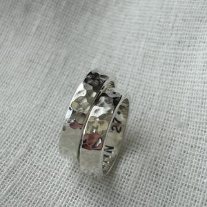 May include: Two silver rings with a hammered texture. The ring on top has the inscription "27" and "N" on the side.