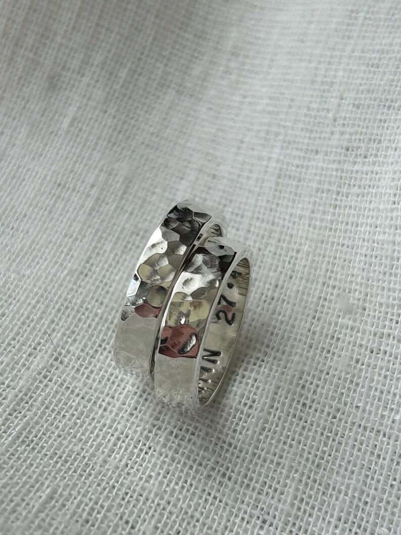 May include: Two silver rings with a hammered texture. The ring on top has the inscription "27" and "N" on the side.