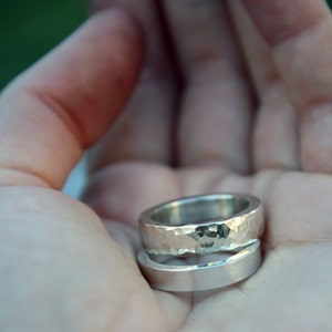 May include: Two silver rings, one with a hammered texture and the other smooth, are stacked on top of each other.