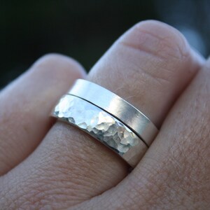 May include: Two silver rings, one with a hammered texture and the other smooth, worn on a finger.