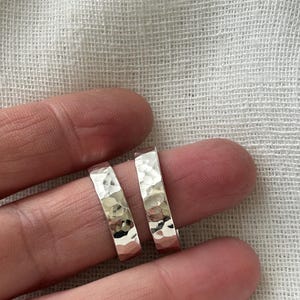 May include: Two silver hammered rings, one slightly larger than the other, are shown on a finger.