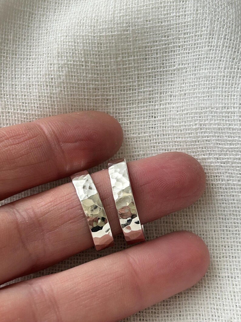 May include: Two silver hammered rings, one slightly larger than the other, are shown on a finger.