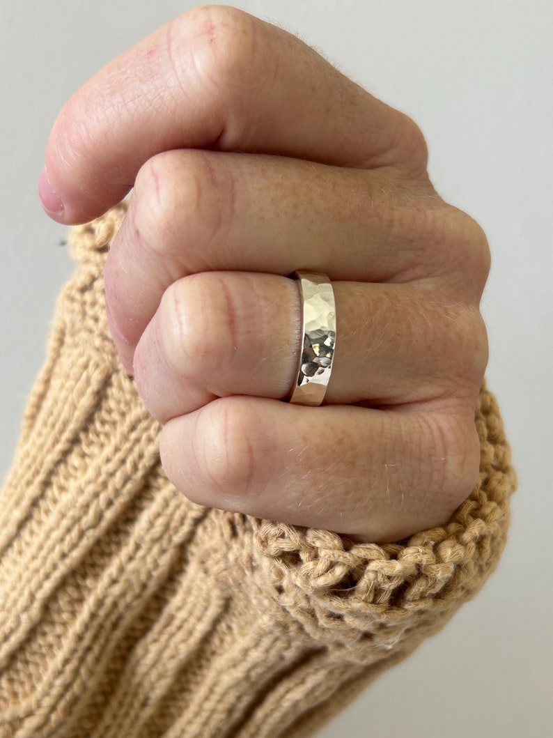 May include: A silver hammered band ring worn on a hand. The ring is wide and has a textured surface.
