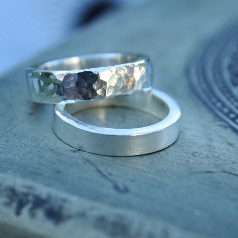May include: Two silver wedding bands. One band has a hammered texture, while the other is smooth and polished.