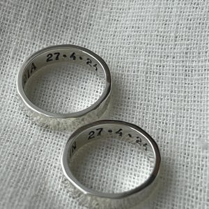 May include: Two silver rings with a hammered texture. The rings are engraved with the date "27.4.25".