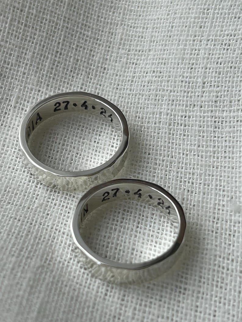 May include: Two silver rings with a hammered texture. The rings are engraved with the date "27.4.25".