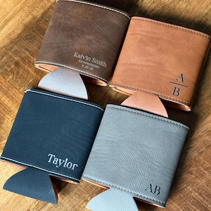 May include: Four personalized leather drink holders in brown, tan, navy, and gray. Each holder has a different name or initials engraved on it. The brown holder says "Kalvin Smith, Groomsman, 9.20.26". The tan holder has "A/B". The navy holder says "Taylor". The gray holder has "AB".
