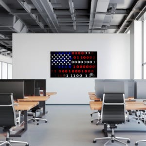 Puede incluir: Una obra de arte digital que representa la bandera estadounidense, con las estrellas y las rayas reemplazadas por c&oacute;digo binario. La obra se exhibe en una pared blanca en un entorno de oficina moderno, con escritorios y monitores de computadora visibles.