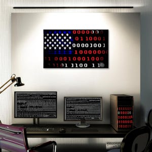 Puede incluir: Una impresi&oacute;n de arte digital de la bandera estadounidense, representada en c&oacute;digo binario, cuelga sobre un escritorio con dos monitores de computadora y una computadora de escritorio. Las estrellas y las rayas de la bandera est&aacute;n representadas por d&iacute;gitos binarios blancos y rojos.