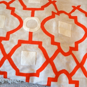 May include: A white throw blanket with a geometric pattern in orange. The pattern is a repeating design of squares and circles.