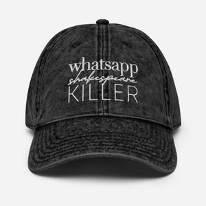 Op de afbeelding: Een zwarte baseballcap in vintage-stijl met de tekst "whatsapp shakespeare KILLER" in het wit geborduurd. De cap heeft een gebogen klep en een knoop aan de bovenkant. De stof heeft een versleten, vervaagde uitstraling.
