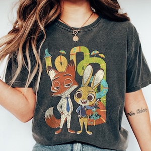 May include: Dark grey t-shirt with a cartoon fox and rabbit from Zootopia. The fox is in a suit and tie, and the rabbit is in a police uniform. The word "Zootopia" is in the background.
