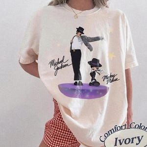 Puede incluir: Camiseta Comfort Colors color marfil con un gr&aacute;fico de Michael Jackson y Mickey Mouse. El dise&ntilde;o incluye el texto "Michael Jackson" y "Mickey Mouse" en escritura cursiva. La camiseta tiene un corte holgado.