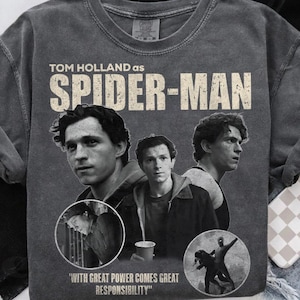 May include: Gray, vintage-style Spider-Man t-shirt featuring Tom Holland. The design includes multiple images of the actor, the words "TOM HOLLAND AS SPIDER-MAN," and the quote "WITH GREAT POWER COMES GREAT RESPONSIBILITY."