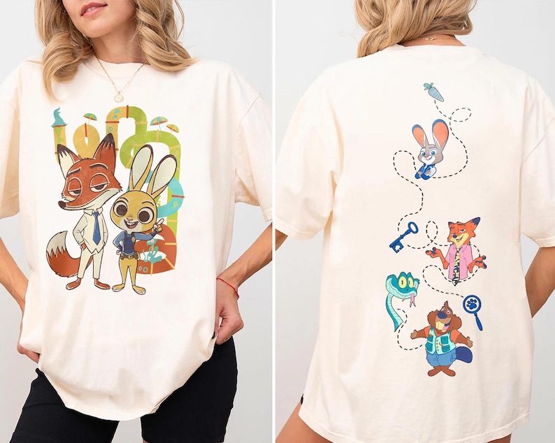 May include: Cream-colored t-shirt featuring cartoon characters of a fox and a rabbit. The front design shows the characters in suits, while the back has a dotted line with other characters. The shirt is a relaxed fit.