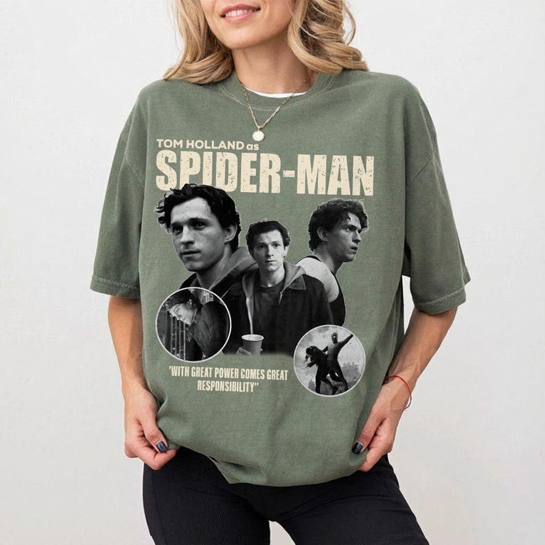 May include: Olive green t-shirt featuring Tom Holland as Spider-Man. The design includes three images of Holland, the words "SPIDER-MAN" in large letters, and the quote "WITH GREAT POWER COMES GREAT RESPONSIBILITY."