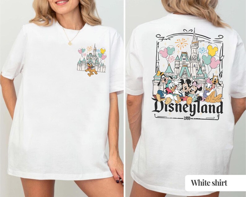 Pode incluir: Camiseta branca com um gr&aacute;fico da Disneyland. A frente mostra Pluto correndo em frente a um castelo com bal&otilde;es. A parte de tr&aacute;s apresenta um gr&aacute;fico maior do castelo da Disneyland com Mickey, Minnie e amigos, com o texto 'Disneyland 1955'.