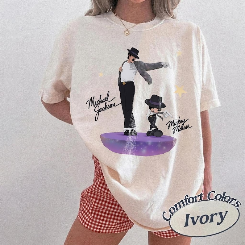 Puede incluir: Camiseta Comfort Colors color marfil con un gr&aacute;fico de Michael Jackson y Mickey Mouse. El dise&ntilde;o incluye el texto "Michael Jackson" y "Mickey Mouse" en escritura cursiva. La camiseta tiene un corte holgado.