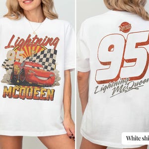 May include: White t-shirt featuring a distressed graphic of Lightning McQueen, the number 95, and the text "Lightning McQueen." The front design includes a checkered flag and a sunburst. The back of the shirt displays a large "95" and the text "Lightning McQueen."