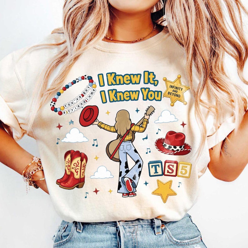 Peut inclure: Un t-shirt cr&egrave;me avec un motif repr&eacute;sentant une personne avec une guitare, des bottes de cow-boy et des chapeaux. Le texte indique I Knew It, I Knew You, Infinity and Beyond et TS5. On y voit aussi un bracelet de perles, des nuages et des &eacute;toiles.