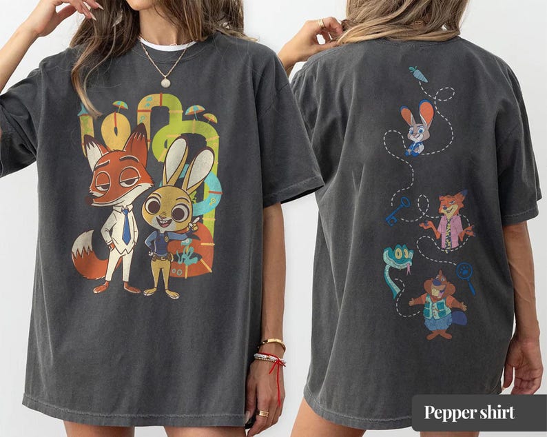 May include: Dark gray t-shirt featuring a colorful graphic of a fox and a rabbit, with the text "Pepper shirt" at the bottom. The back of the shirt has cartoon characters. The shirt is made of a soft material.