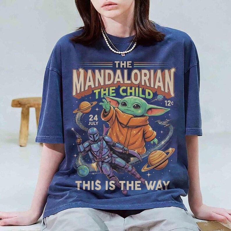 May include: Navy blue t-shirt featuring a graphic from The Mandalorian. The design includes the text "The Mandalorian The Child" with an image of Grogu and the Mandalorian. The shirt also has the text "This is the Way".