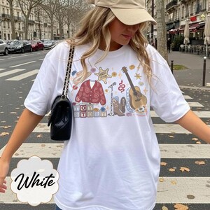 May include: A white t-shirt featuring a graphic print with a brown cowboy hat, a red paisley cardigan, a sheriff star badge labeled Sheriff Taylor, a microphone, a brown acoustic guitar, a cowboy boot, and blocks spelling out TOY STORY.